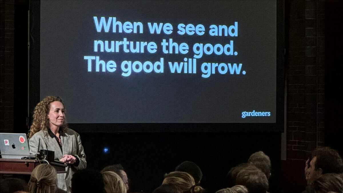 Spreker van Gardeners tijdens een presentatie voor publiek, met op het scherm de tekst 'When we see and nurture the good. The good will grow.'